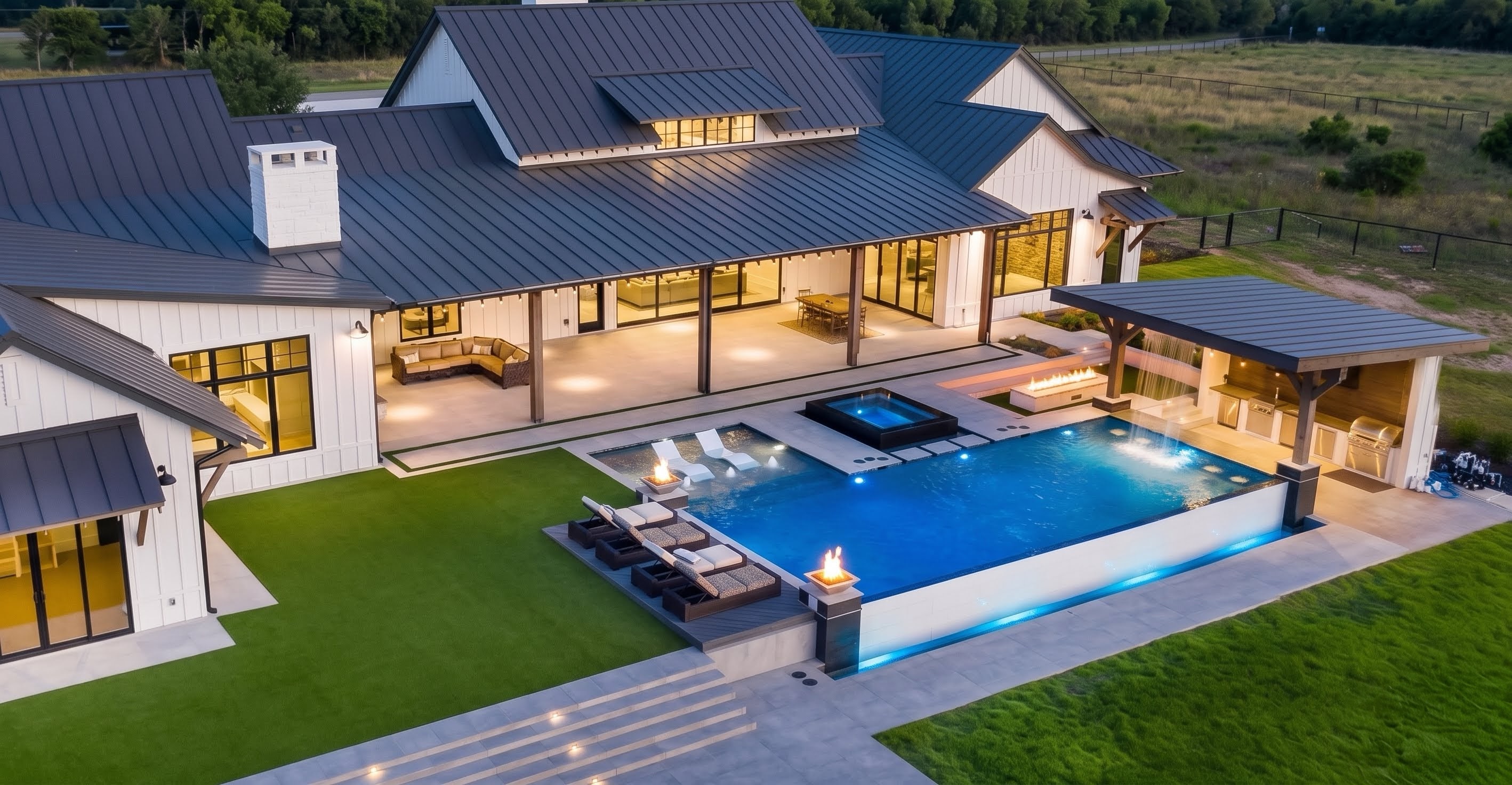 Aerial view of a modern Texas estate with infinity pool and fire bowls at dusk